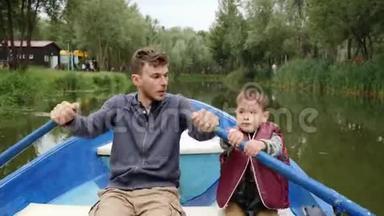 年轻的父亲和他的小儿子一<strong>起坐</strong>船在绿树丛中。 快乐的一家人周末在湖边公园玩得开心。